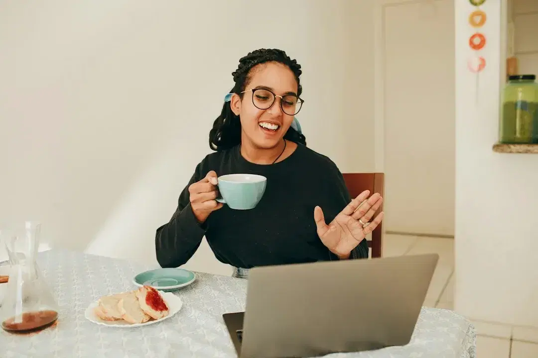 Uma mulher a ler no portátil à mesa da cozinha com uma chávena de café